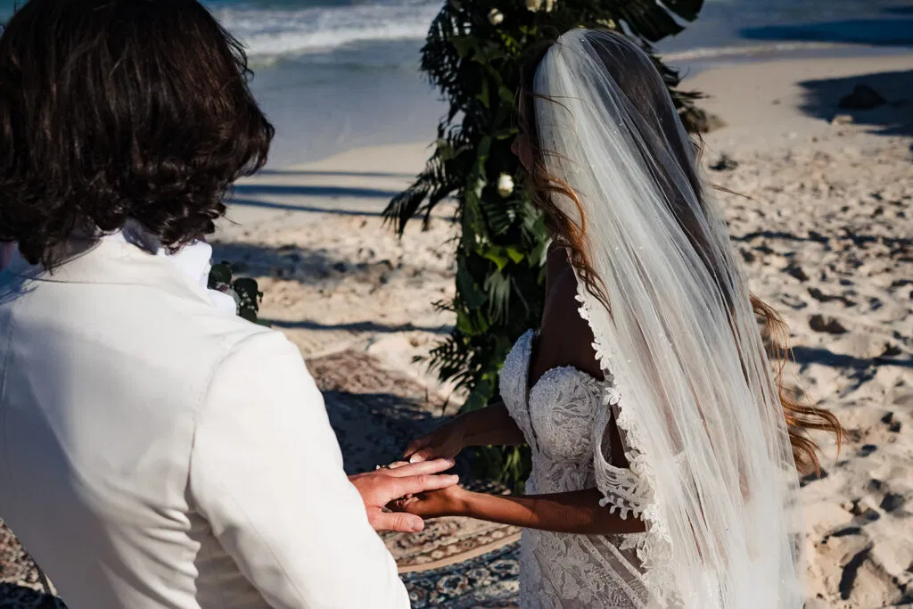 Intimate beach wedding ceremony in Tulum with bride and groom exchanging vows under tropical palm trees on white sand