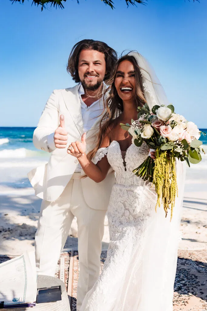 Newlywed couple celebrating beach wedding in Tulum Mexico with tropical bouquet and ocean backdrop