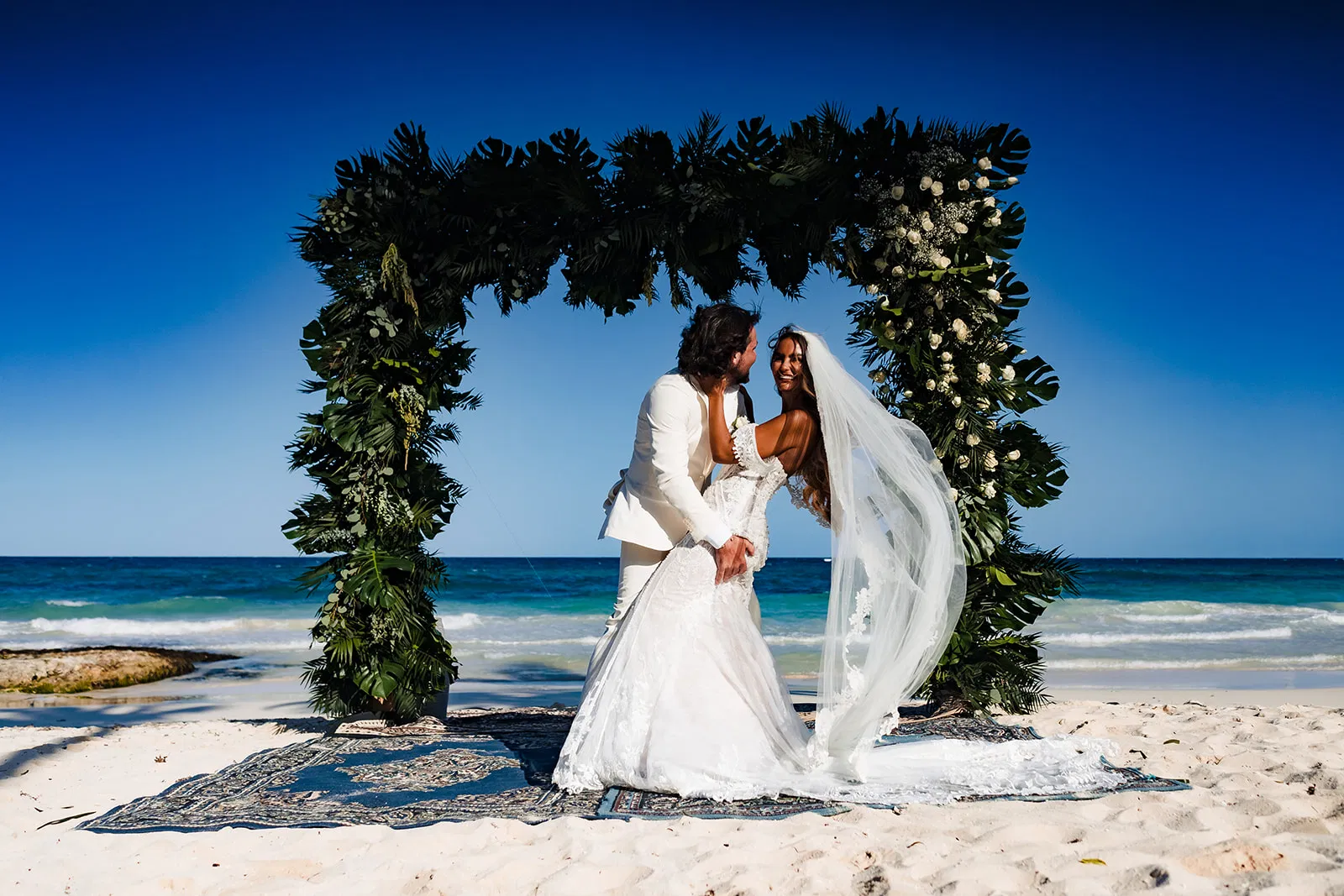 Beach wedding ceremony in Tulum Mexico with bride and groom under tropical floral arch overlooking turquoise Caribbean Sea