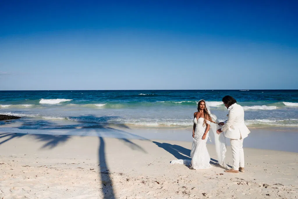 Bride and groom walking hand in hand on pristine Tulum beach with turquoise Caribbean waters and blue sky backdrop