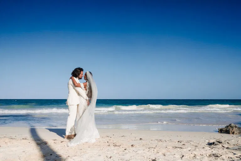 Romantic beach wedding couple kissing on Tulum's pristine white sand beach with turquoise Caribbean Sea backdrop