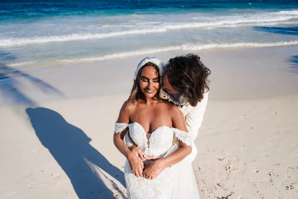 Romantic beach wedding couple embracing on pristine white sand in Tulum Mexico with turquoise Caribbean waters behind them