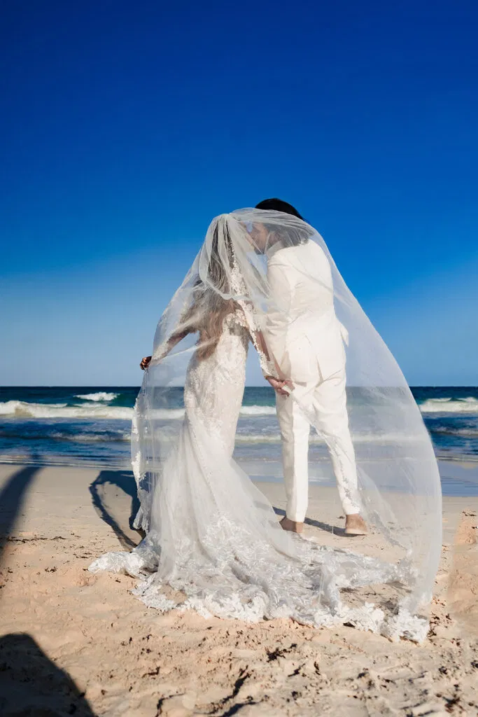 Bride and groom embracing under flowing veil on Tulum beach with turquoise Caribbean Sea - destination wedding photography