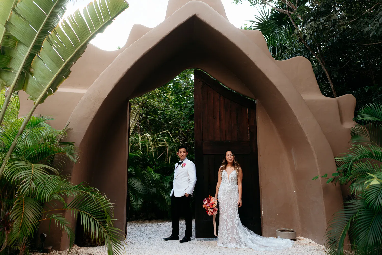 Bride and groom wedding portrait at adobe archway surrounded by tropical palms in Tulum Mexico destination wedding