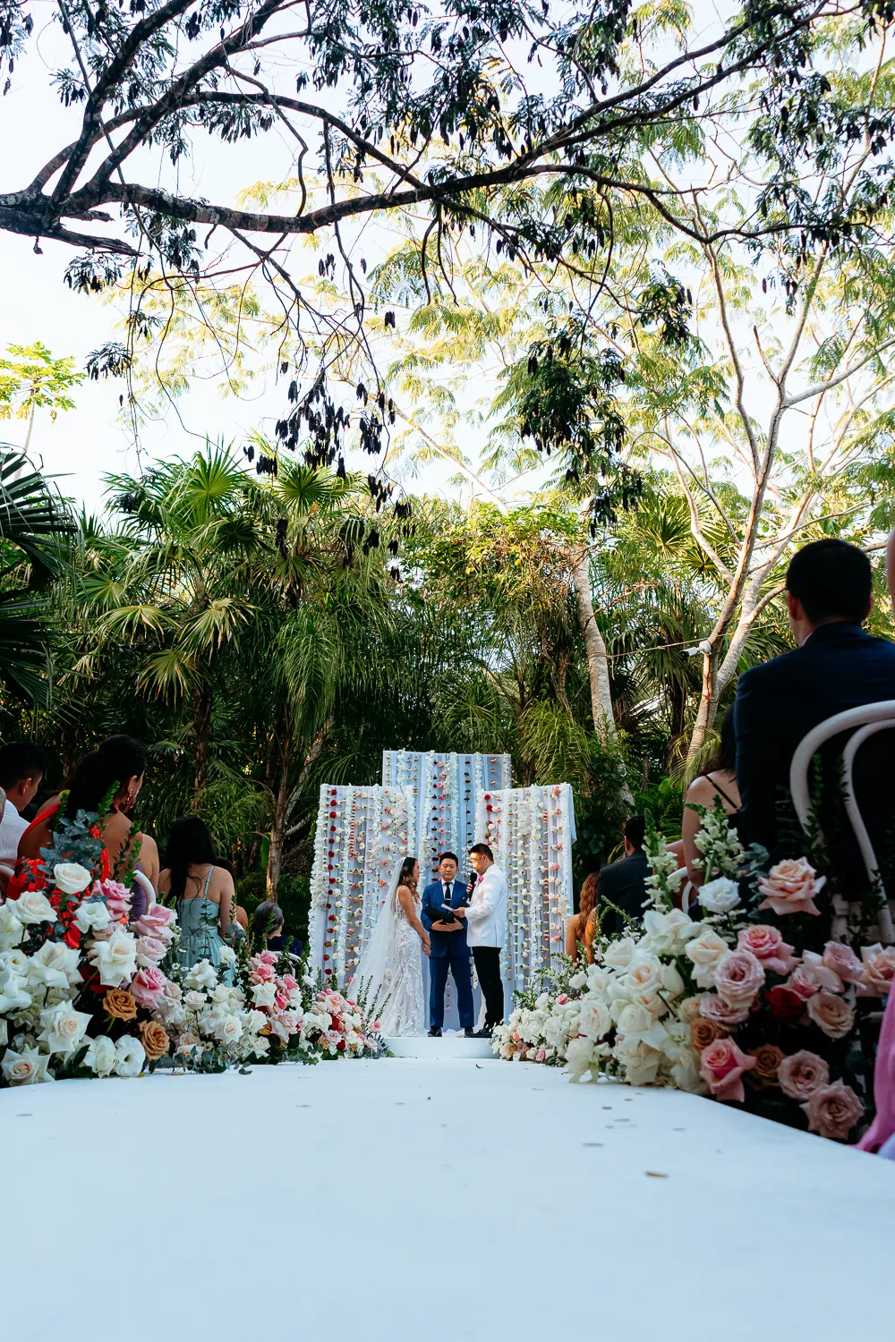 Tulum wedding ceremony with bride and groom exchanging vows under tropical palms with floral aisle decorations