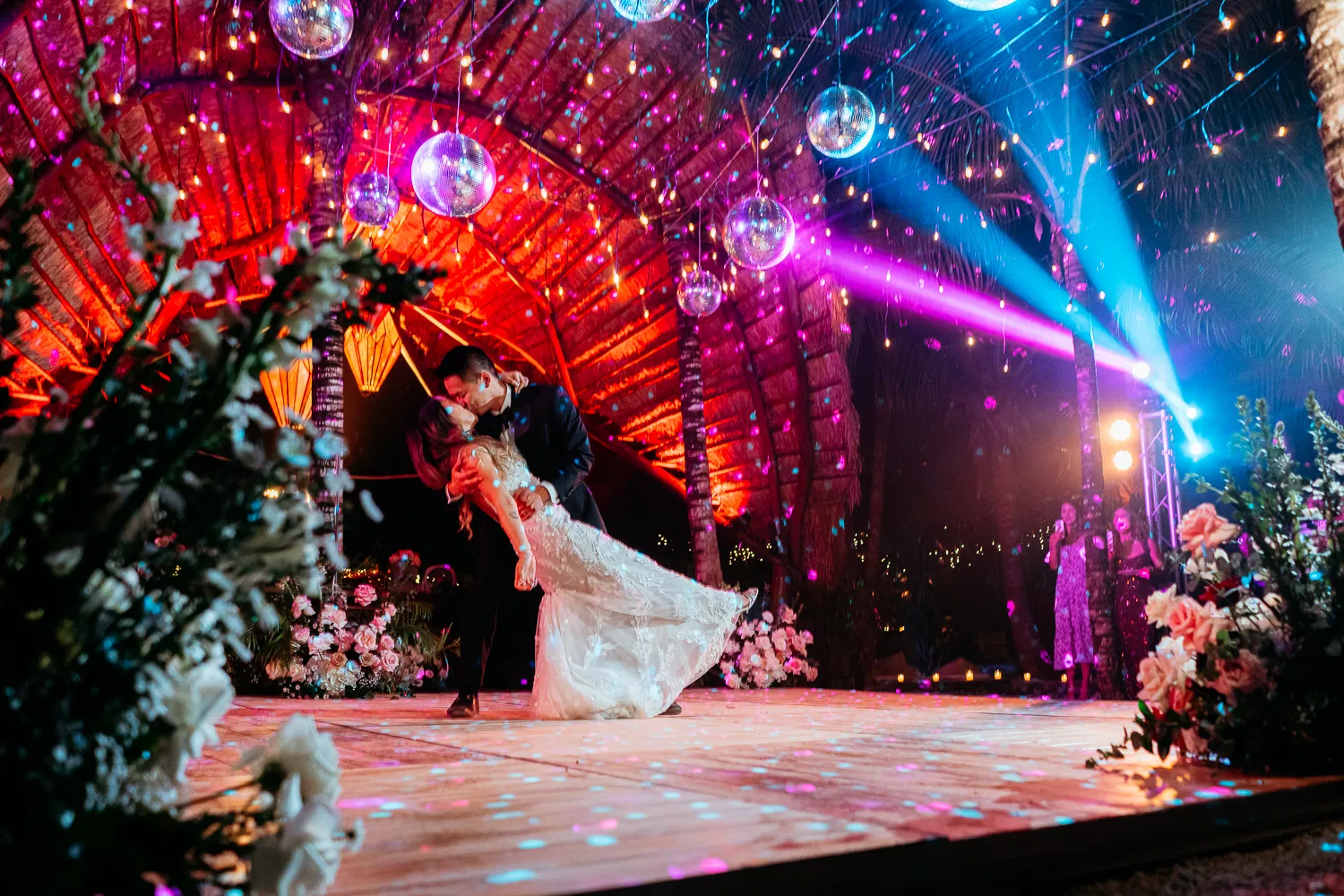 Bride and groom dancing under disco balls with colorful lights at luxury Tulum wedding reception with tropical decor