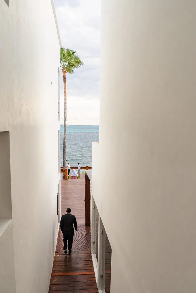 Groom walking down wooden boardwalk pathway to beach wedding ceremony in Tulum Mexico with ocean view