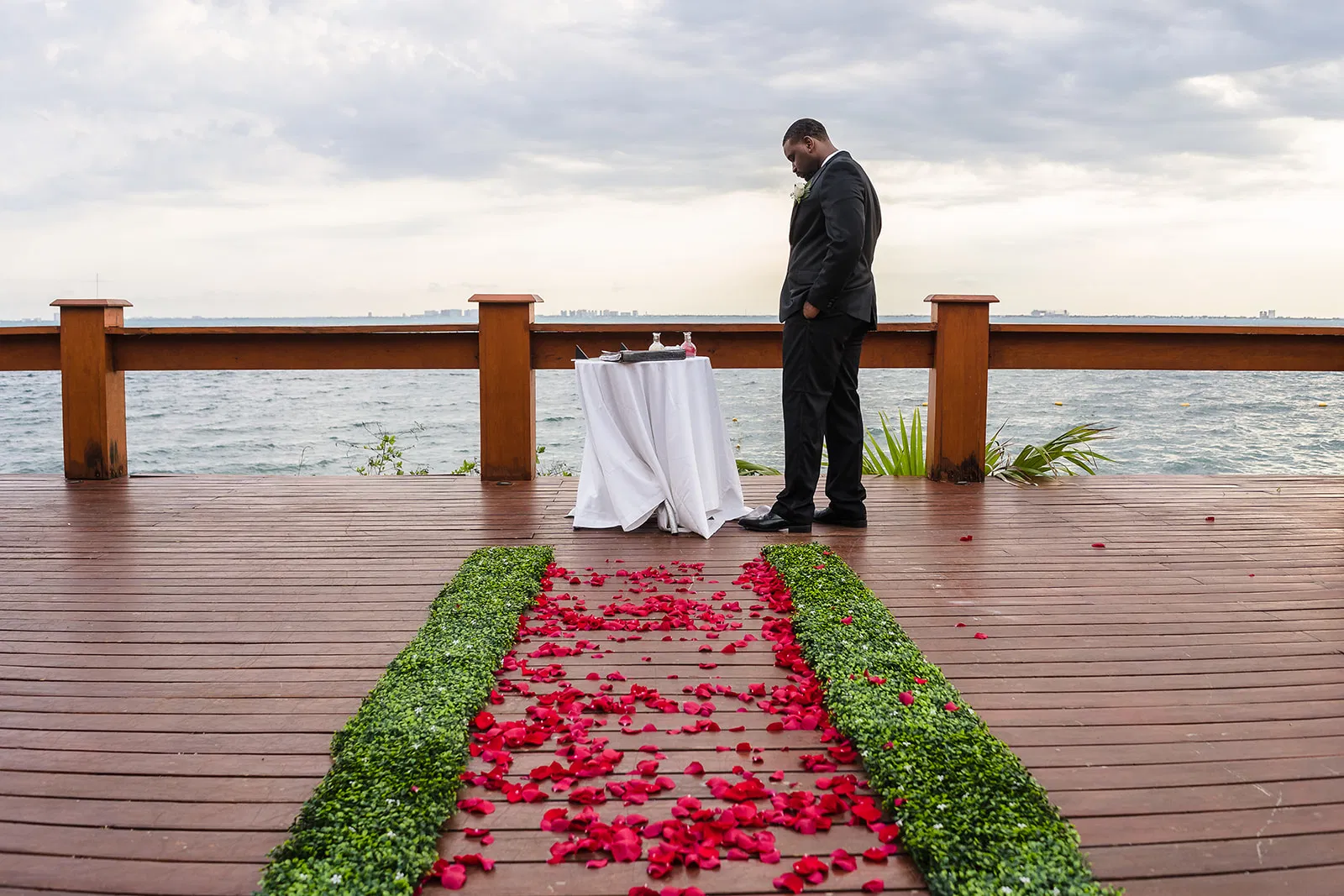 Groom waiting at waterfront wedding ceremony setup with rose petal aisle in Tulum Mexico destination wedding photography