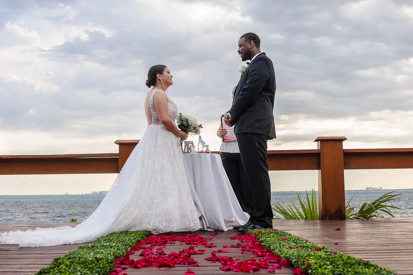 Romantic wedding ceremony on wooden deck overlooking ocean in Tulum Mexico with bride groom and rose petal aisle