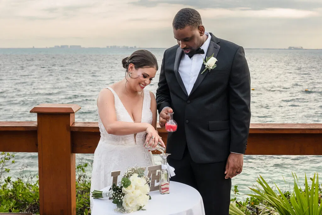 Bride and groom performing sand ceremony at oceanfront Tulum wedding with Caribbean Sea backdrop and tropical plants