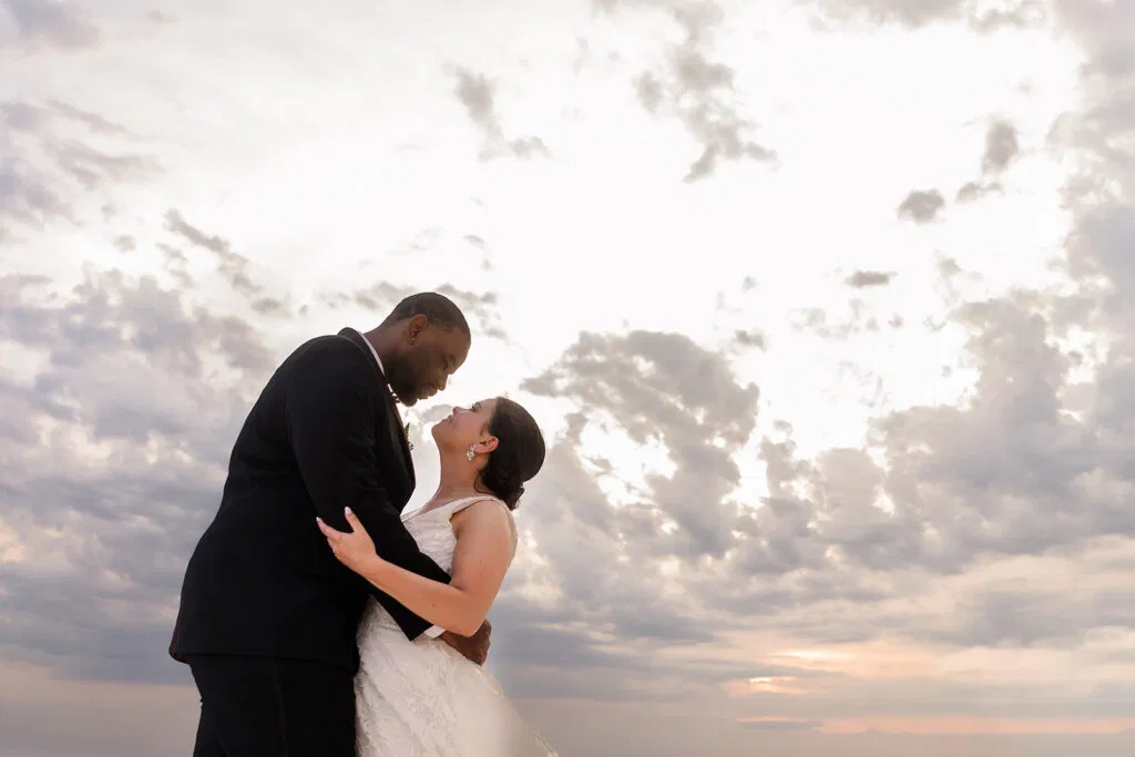 Romantic wedding couple embracing at sunset on Tulum beach with dramatic cloudy sky - destination wedding photography Mexico